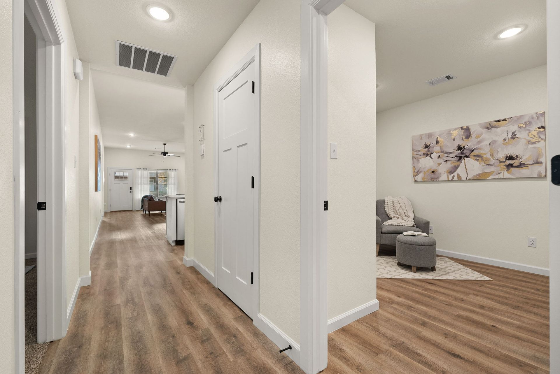 A hallway in a house with hardwood floors and white walls leading to a living room.