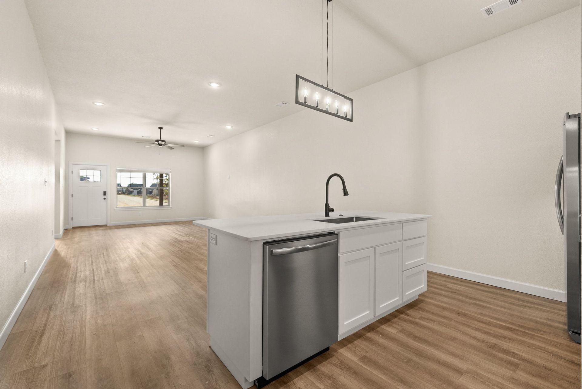 A kitchen with white cabinets , a stainless steel dishwasher , a sink and a refrigerator.