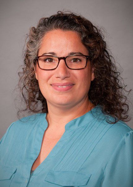 A woman wearing glasses and a blue shirt is smiling for the camera.