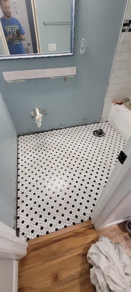 Bathroom with black and white tiled floor, blue walls, and wooden floor. A mirror and sink fixture are visible.