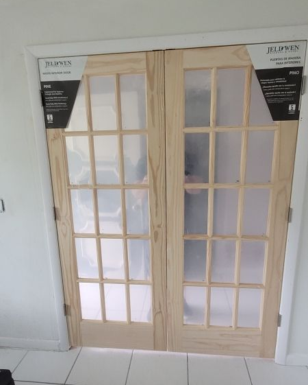 Two unpainted wooden French doors with glass panes, installed in a white door frame.