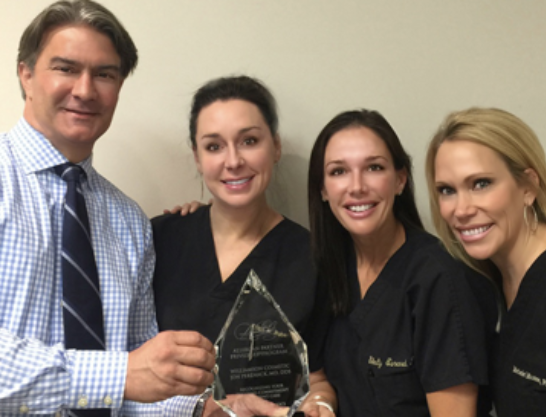 Four people smiling, holding an award. One man in a tie, three women in black tops.