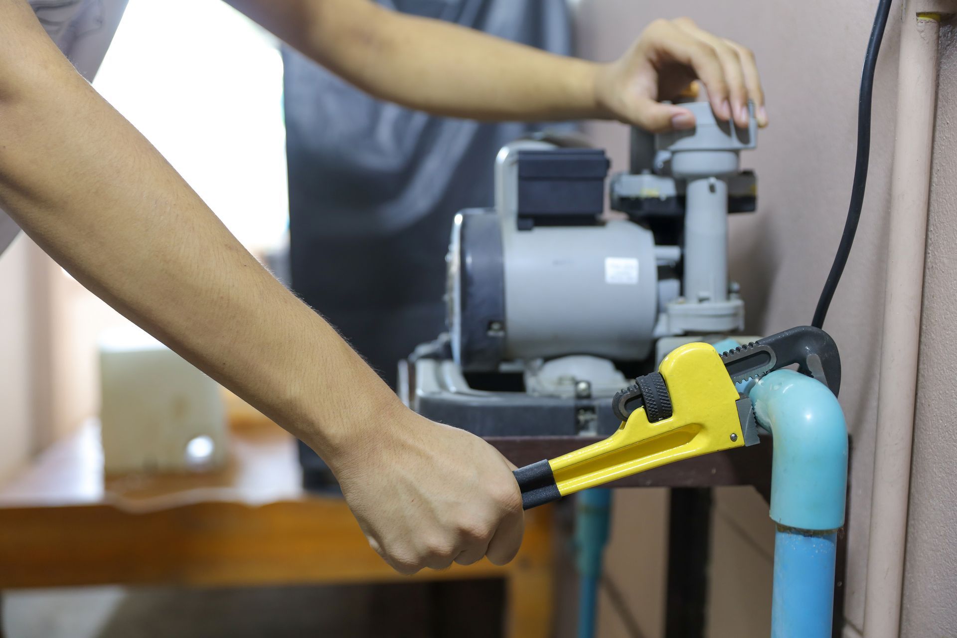 A person uses a yellow pipe wrench to adjust the blue plumbing connected to a gray water pump.