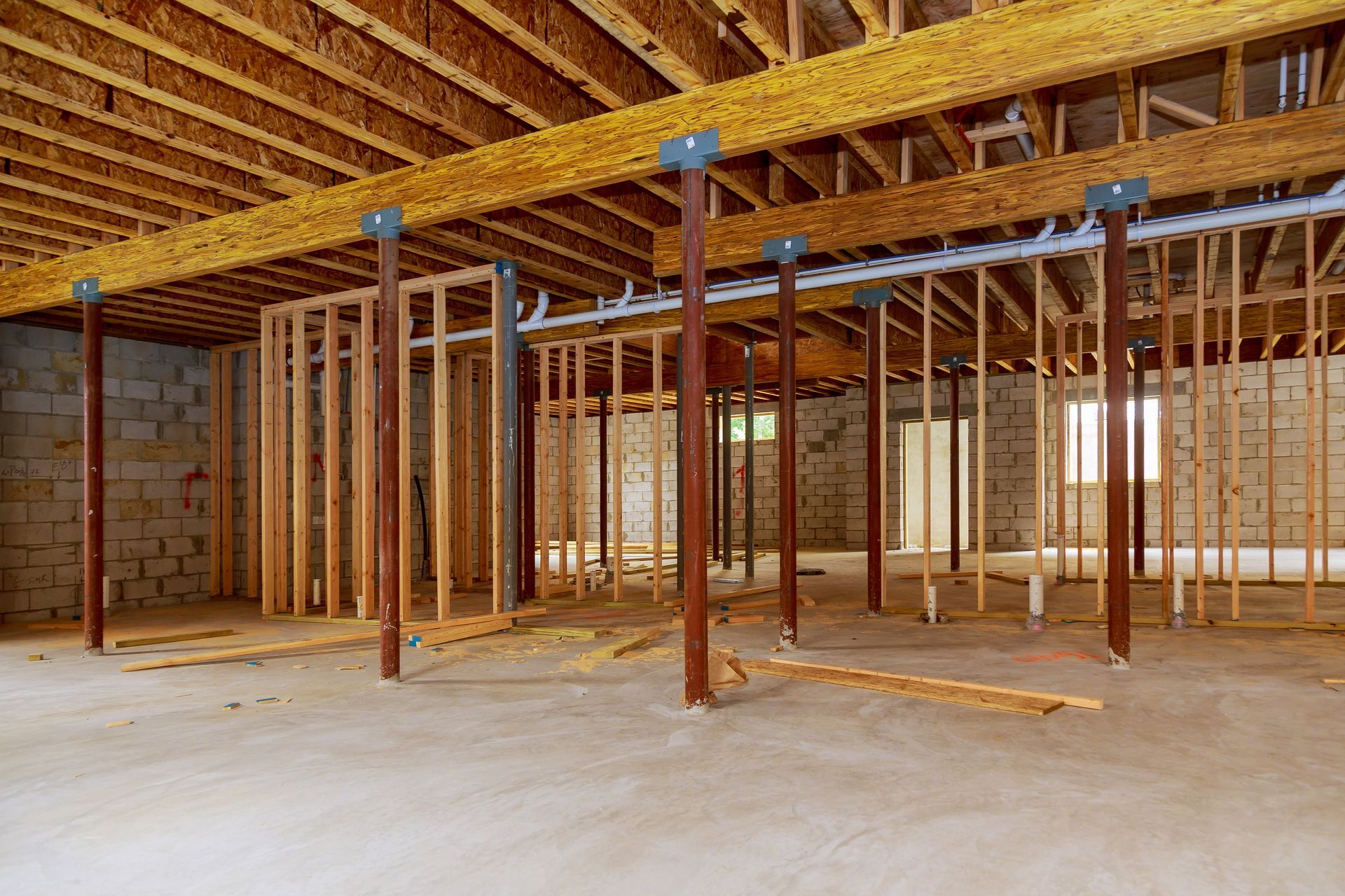 An unfinished basement with exposed wooden joists, metal support columns, and framed walls on a concrete floor.