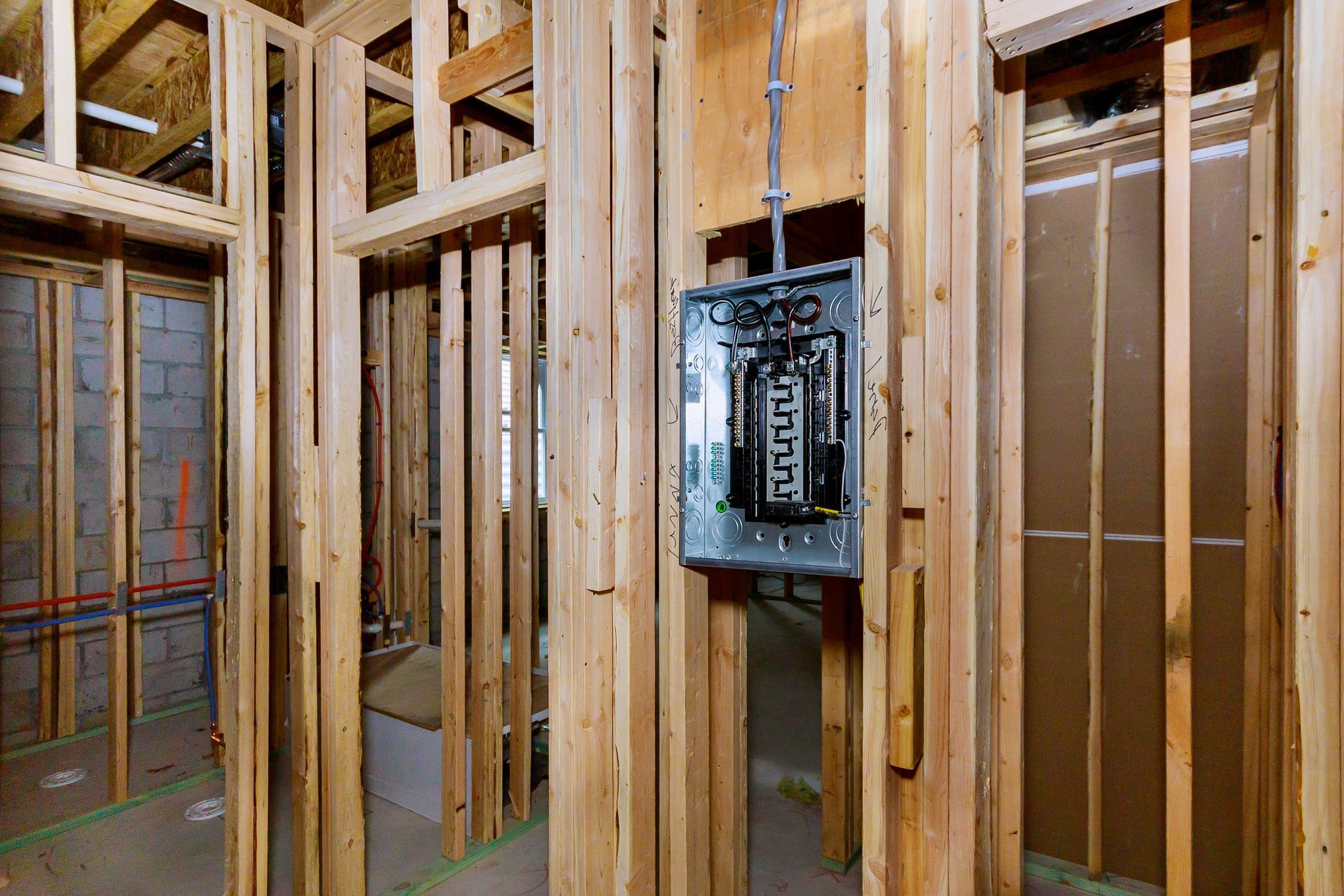 A metal electrical service panel mounted on wooden wall studs inside an unfinished room under construction.