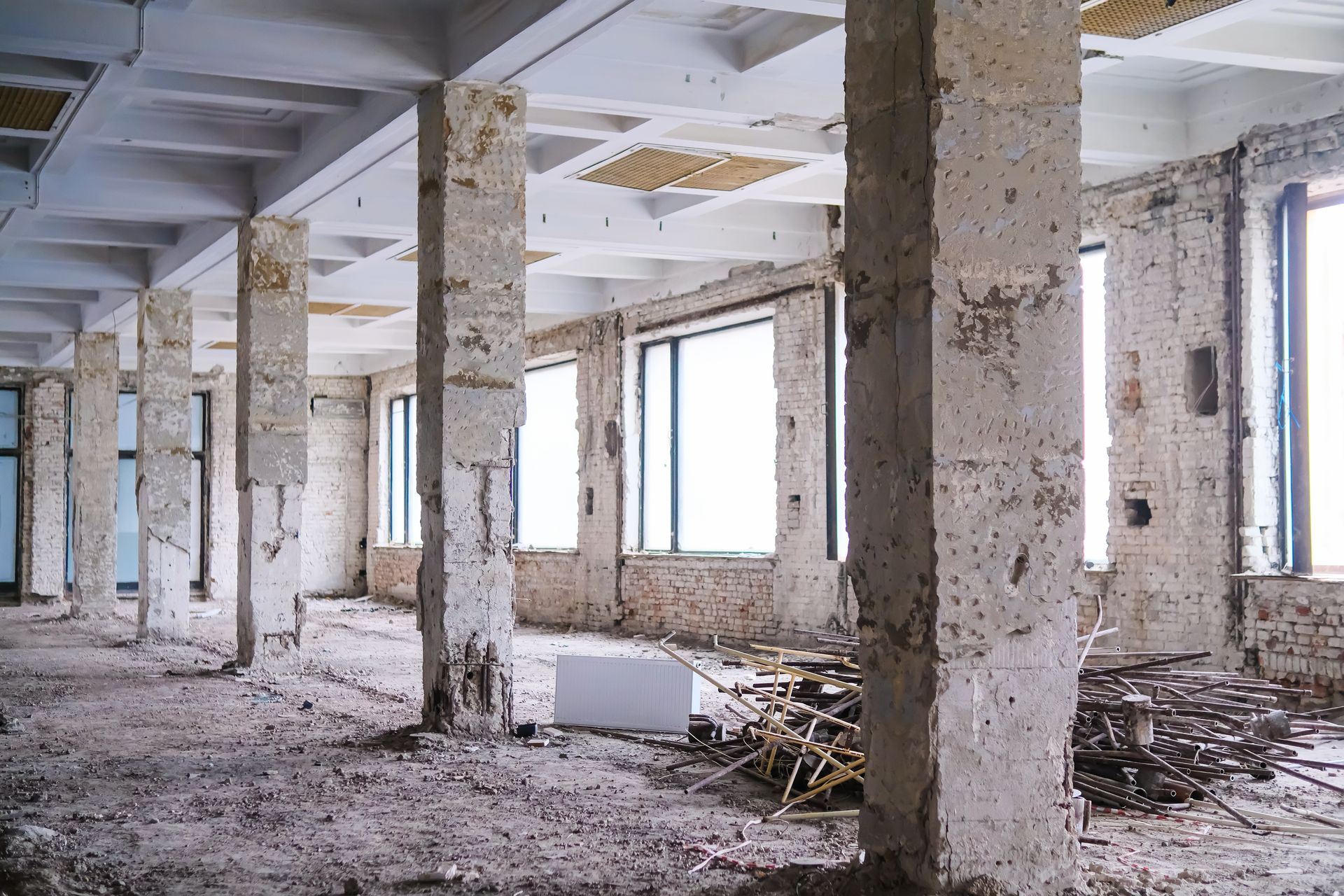 A large, empty industrial loft undergoing renovation with concrete pillars, unfinished walls, and dusty floors.