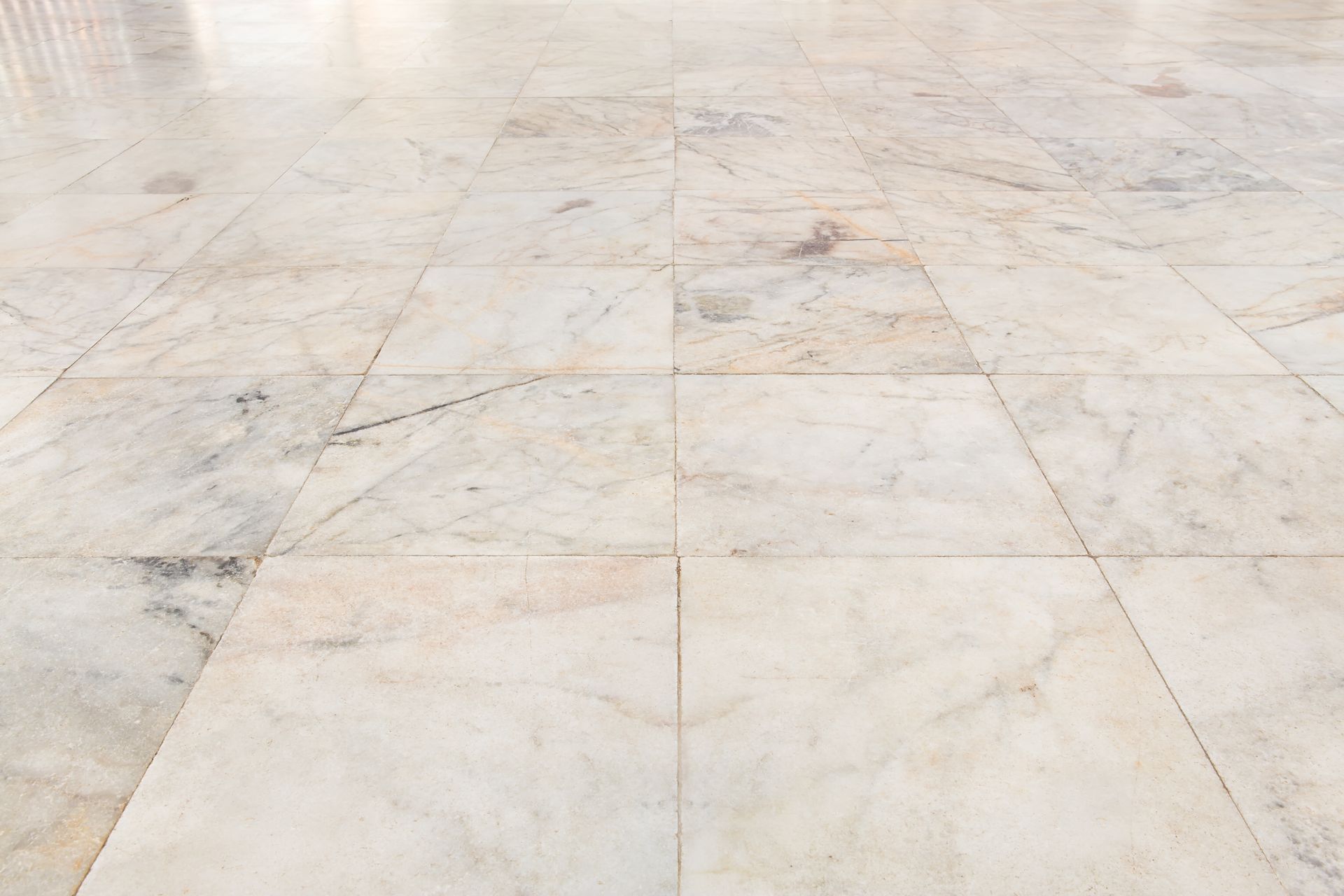 A perspective view of light, beige marble floor tiles with grey veining.