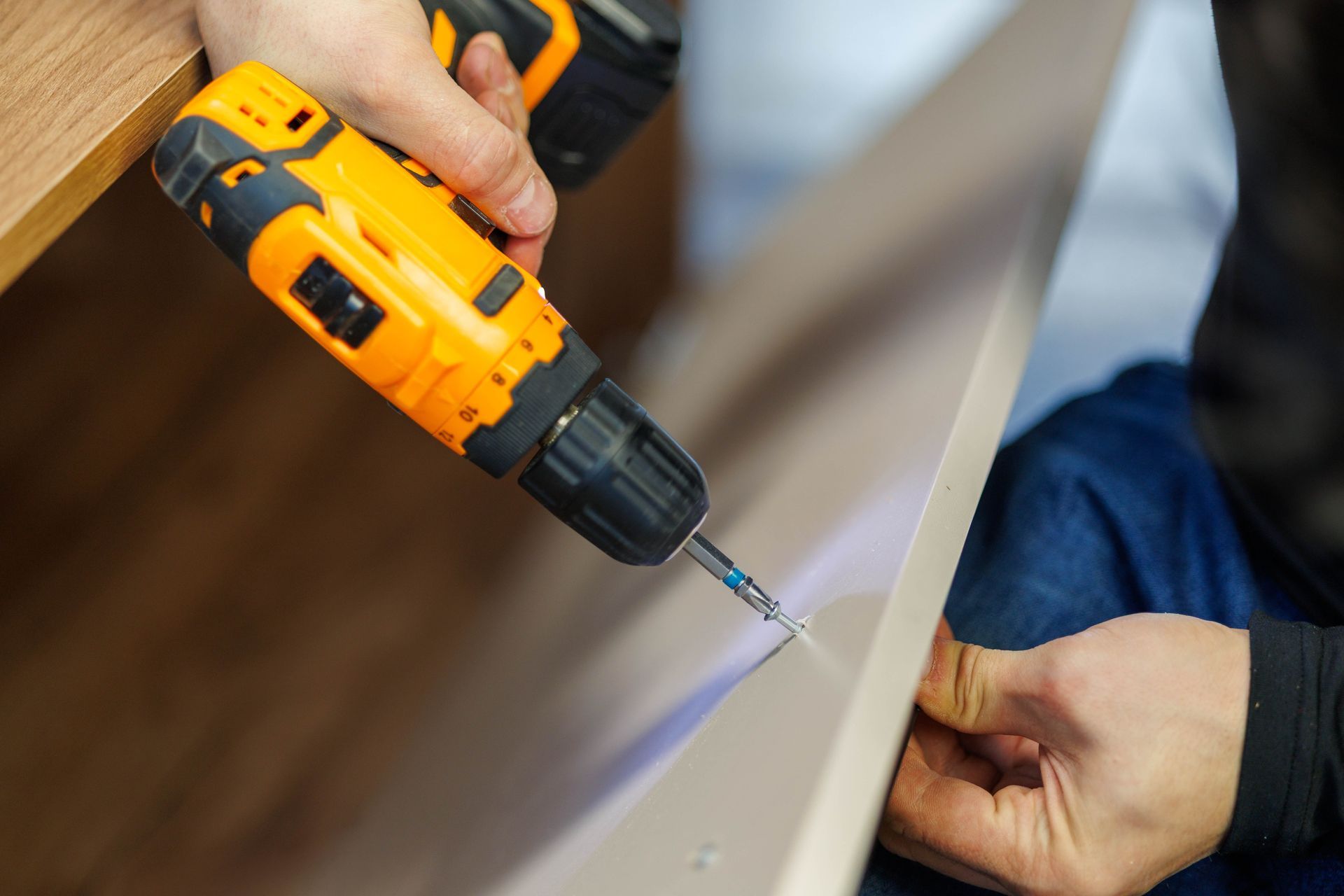 A person uses a yellow electric drill to assemble flat-pack furniture.