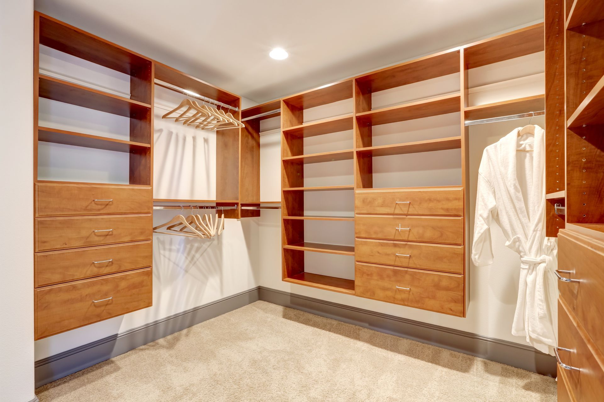 Walk-in closet with warm wood shelves, drawers, and hanging rods, featuring a white robe on a hanger.