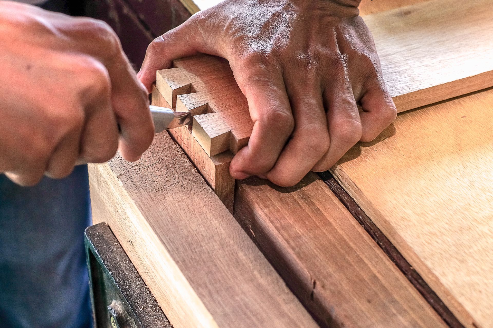 A woodworker uses a chisel to refine dovetail joints on a wooden board.
