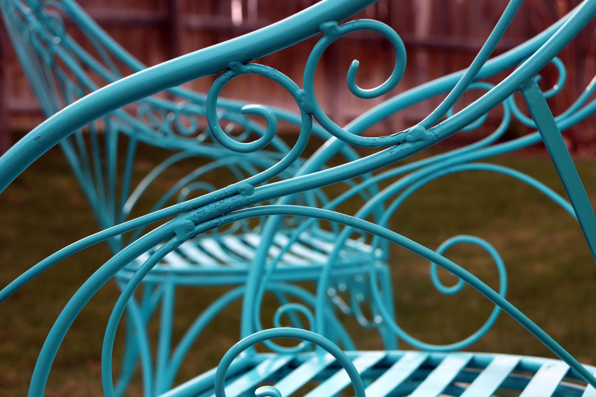 Turquoise wrought iron garden chairs with ornate swirling metalwork sit on a lawn.