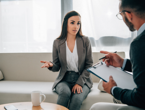 A woman is sitting on a couch talking to another woman.