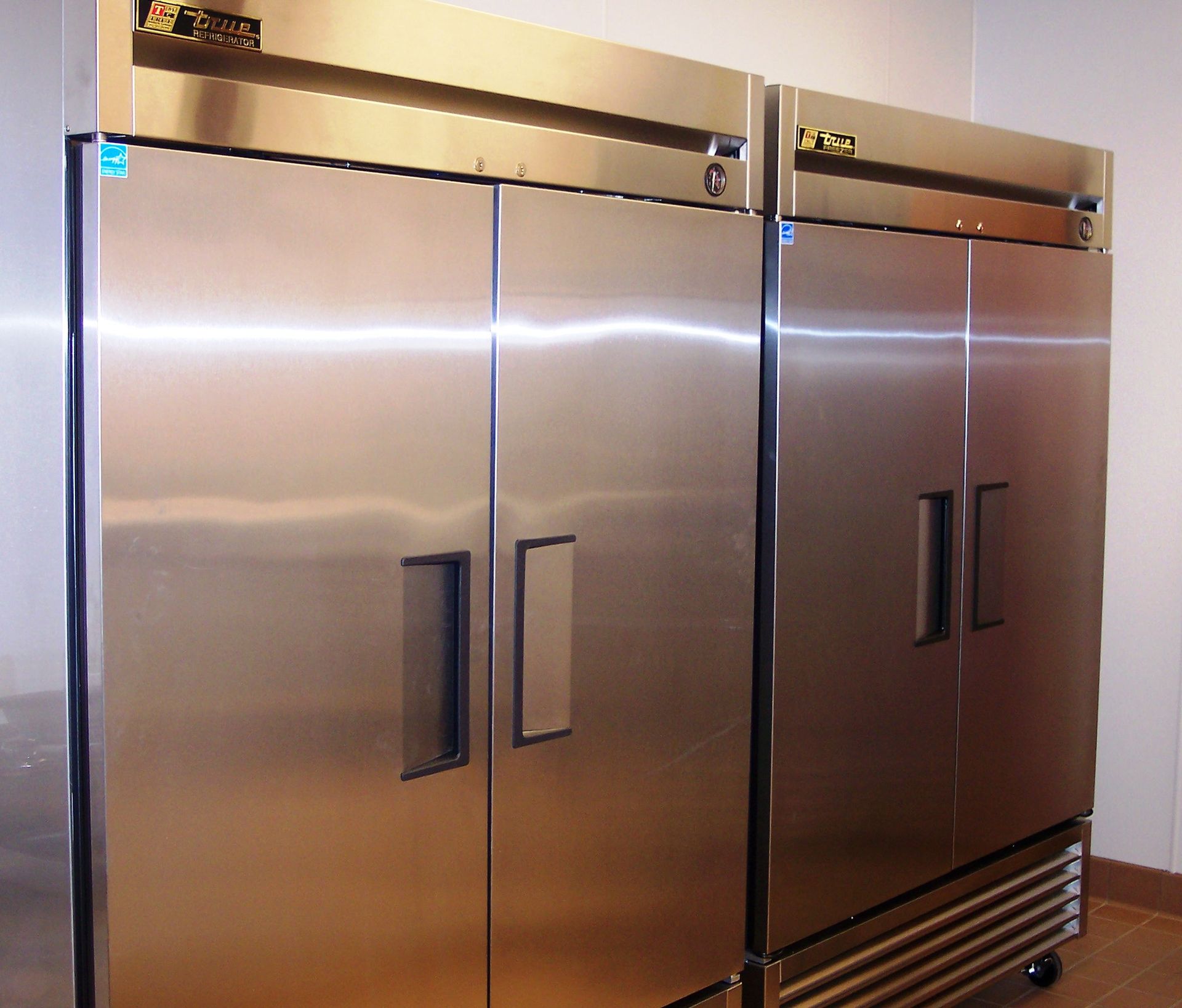 Two large, stainless-steel commercial refrigerators standing side-by-side in a kitchen setting.