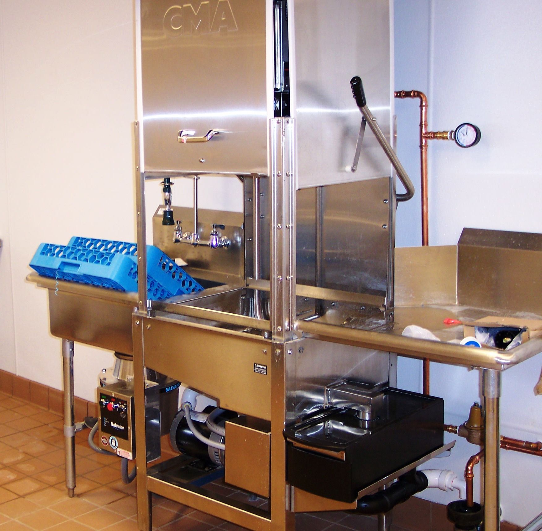 A stainless steel commercial dishwasher in a kitchen setting with a blue plastic rack on the left side.