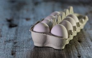 A carton of eggs is sitting on a wooden table.