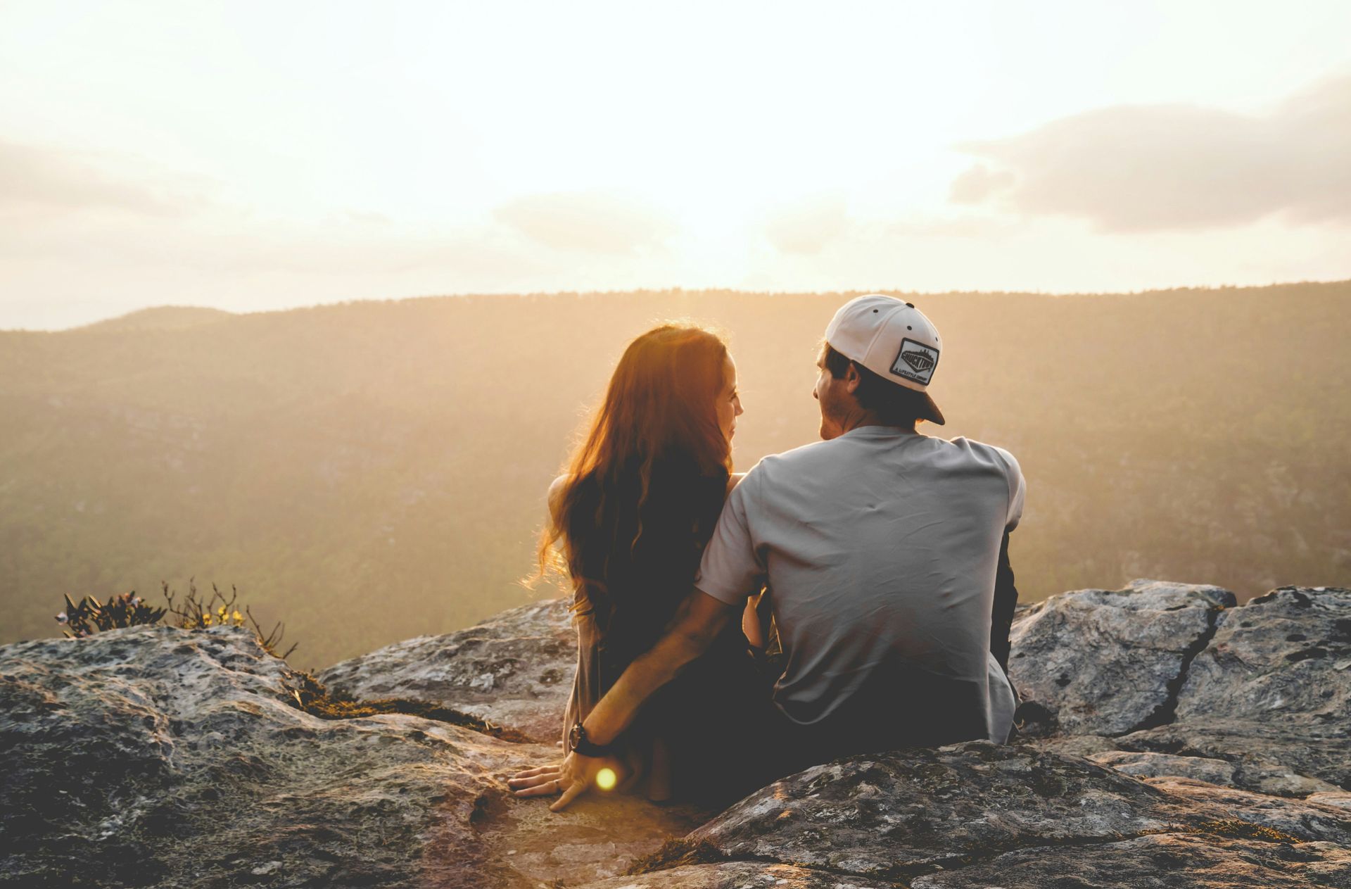 Couple sitting on top of a mountain watching the sunset.