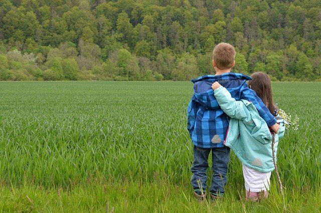 A boy and a girl are standing in a field hugging each other.