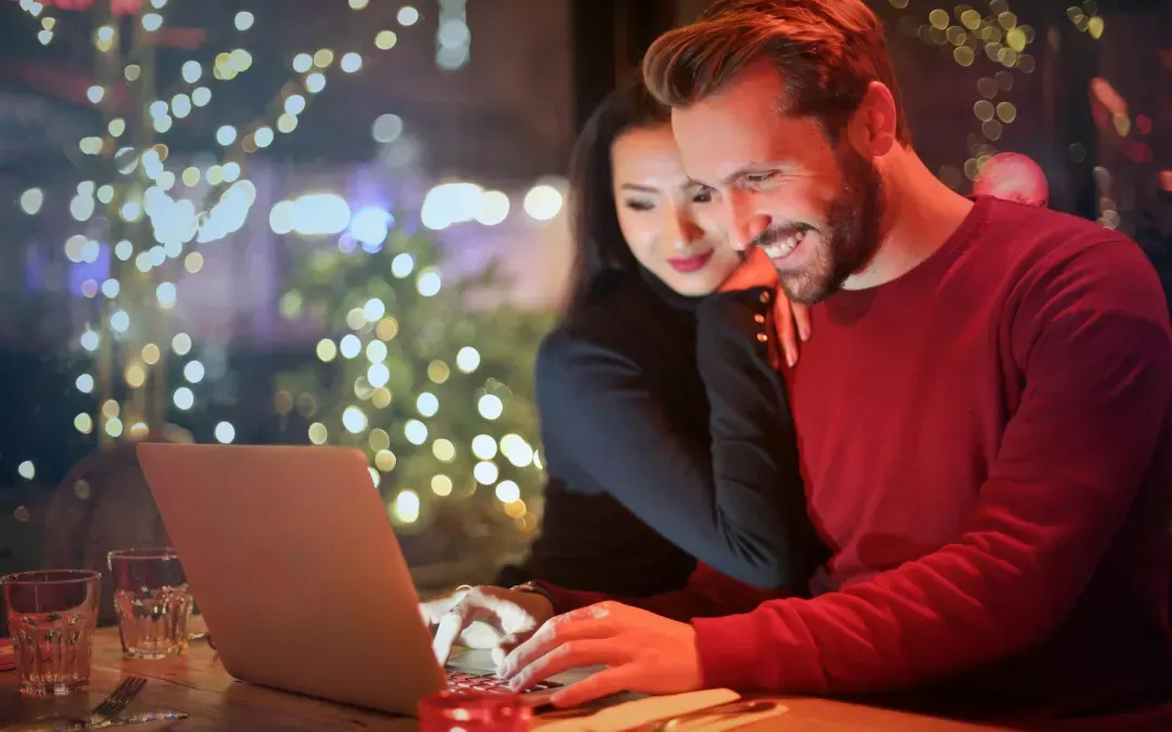 A man and a woman are sitting at a table looking at a laptop computer.