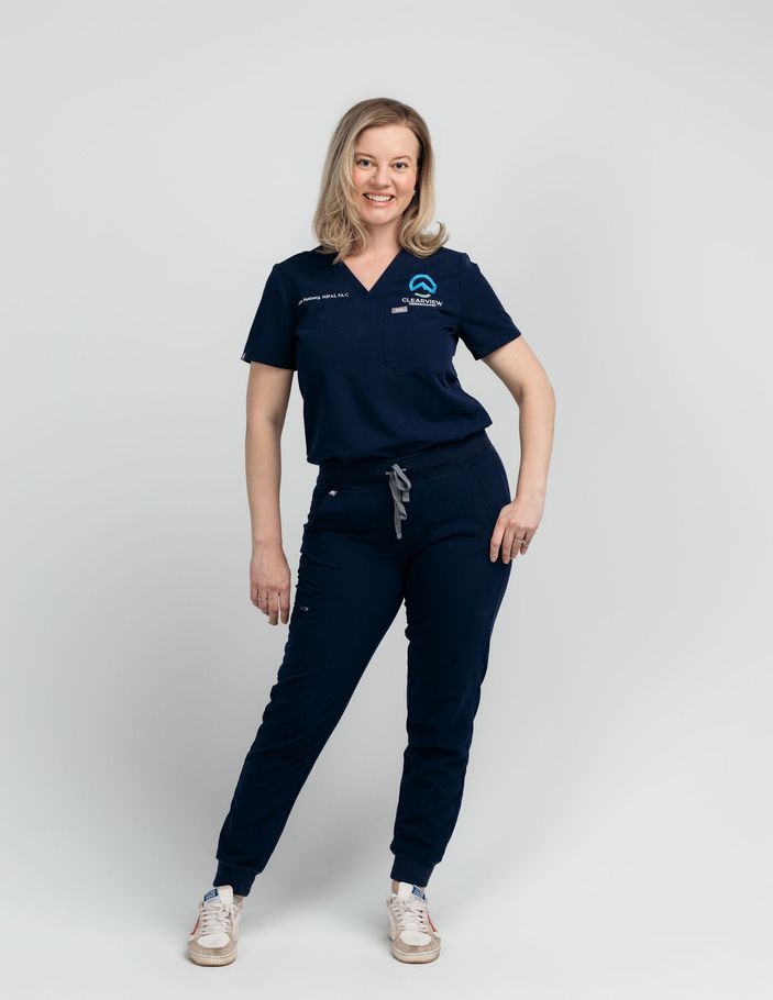 a woman in a blue scrub suit is standing in a hallway with her hands in her pockets .