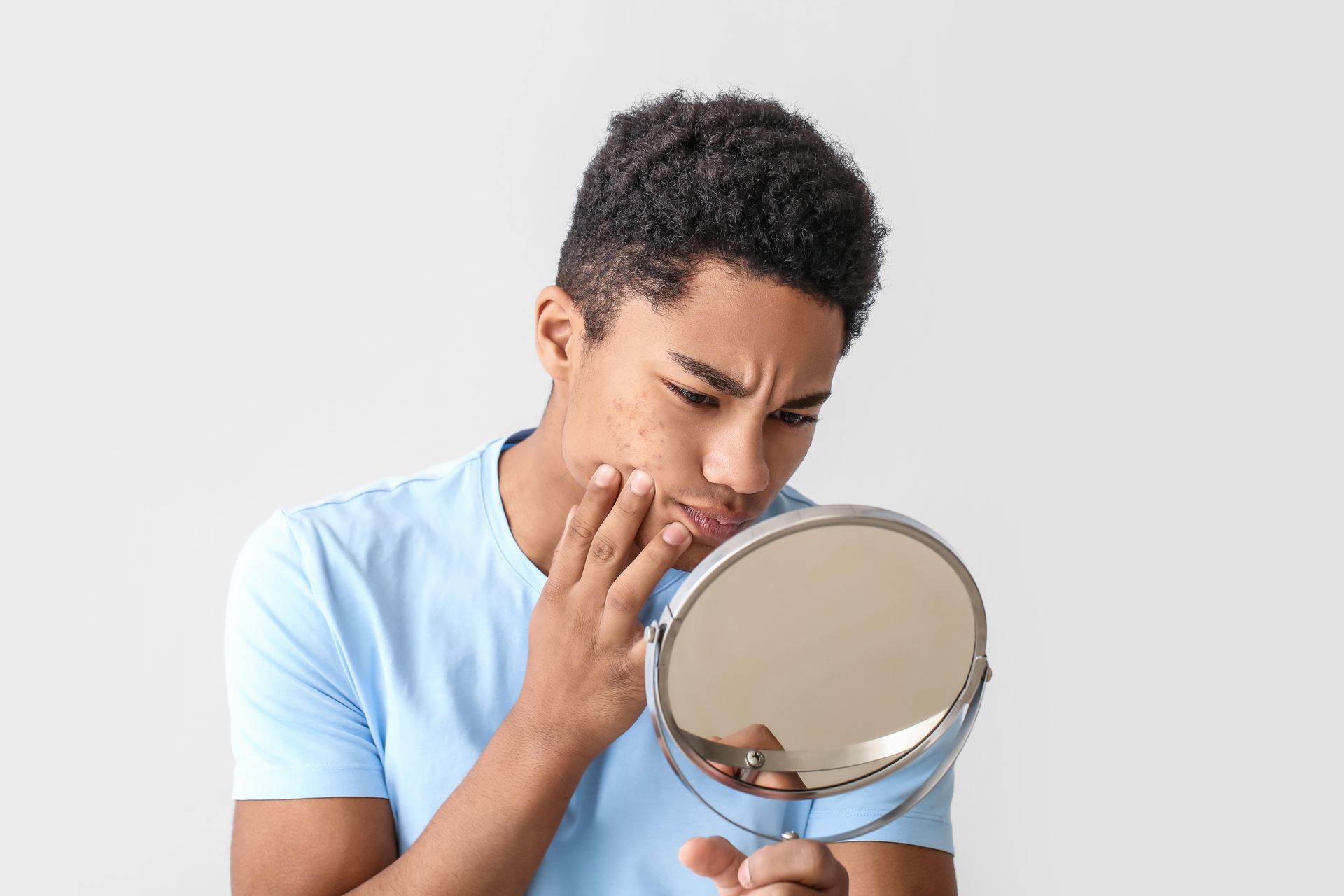 Teenage boy looking at face in a mirror, concerned about acne