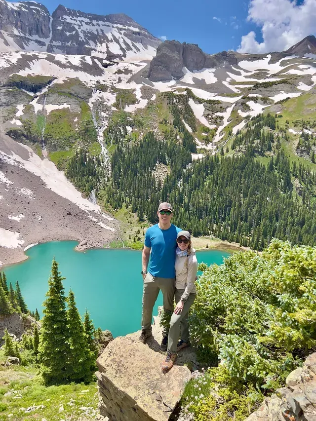 A man and a woman are standing on top of a mountain next to a lake.
