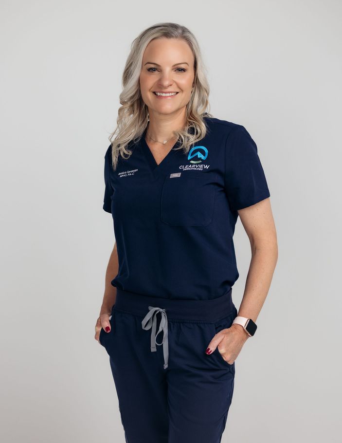 a woman in a blue scrub suit is standing in a hallway with her hands in her pockets .