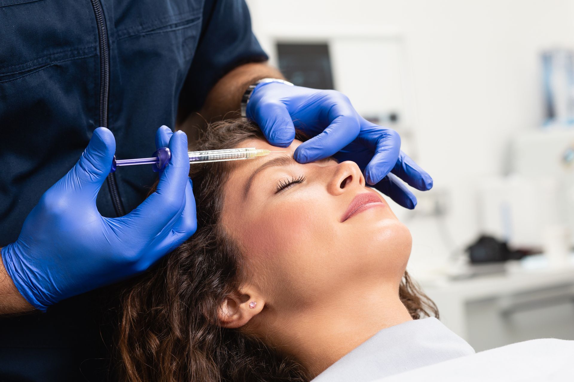 Cosmetic procedure in progress as gloved hands inject above a woman’s eyebrow in a clinic
