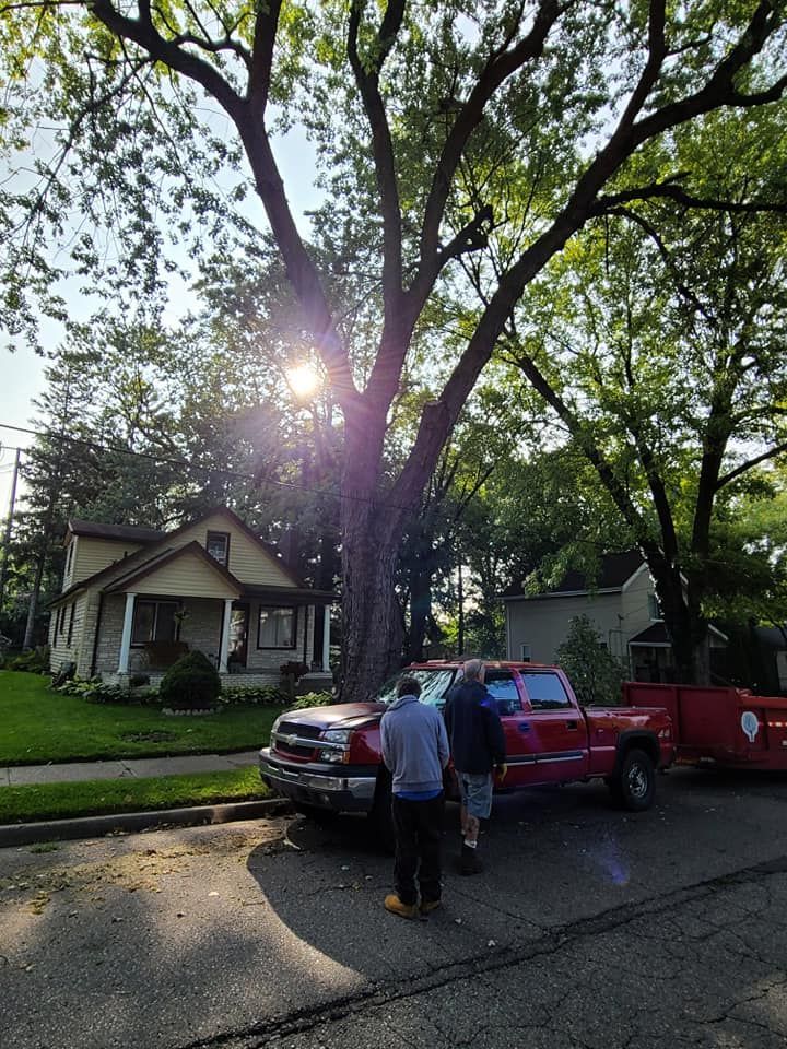 Two men are standing next to a red truck parked in front of a house.