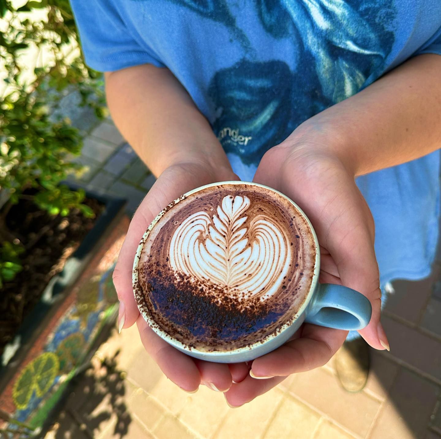 Hands Holding a Blue Mug With a Latte, Brown Cocoa Dusted Edges — Drop In Espresso Bar in Wallsend, NSW