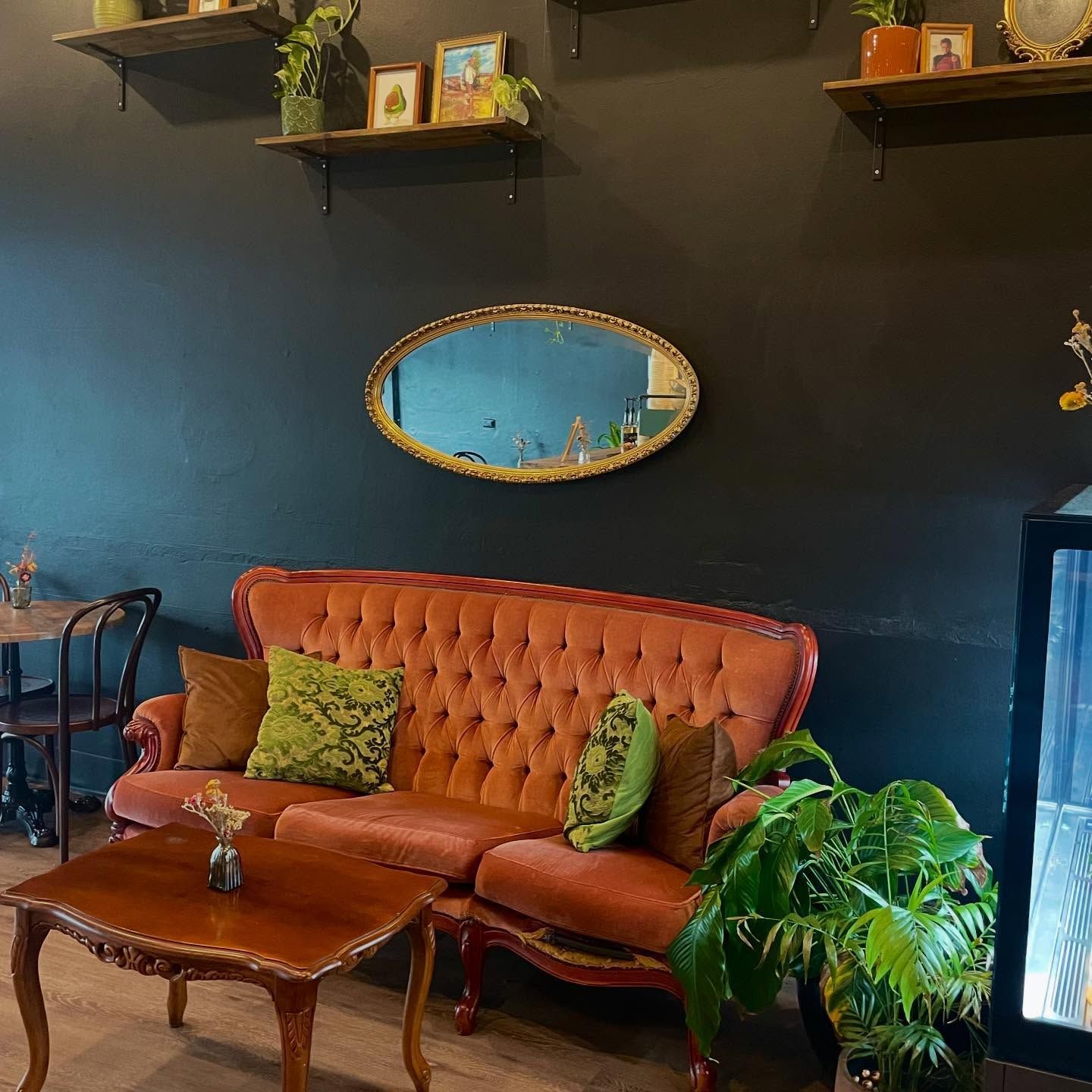 Cozy cafe interior with a velvet orange couch, wooden table, green pillows, and dark blue wall — Drop In Espresso Bar in Wallsend, NSW