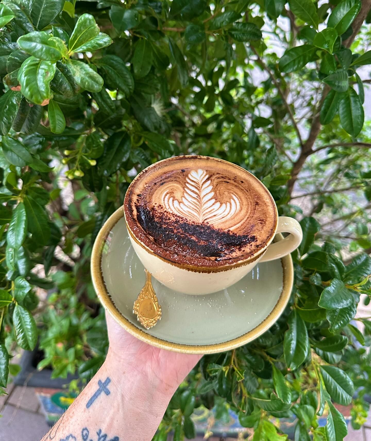 Hand Holding a Cappuccino With Latte Art, on a Saucer — Drop In Espresso Bar in Wallsend, NSW