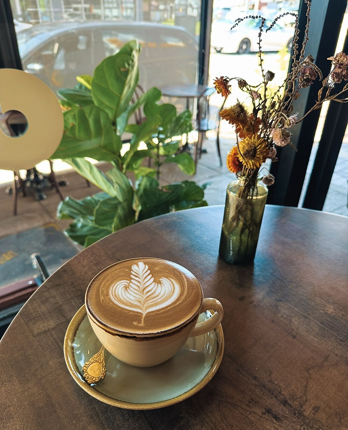 Latte Art in Cup on Saucer, Table. Green Plant — Drop In Espresso Bar in Wallsend, NSW