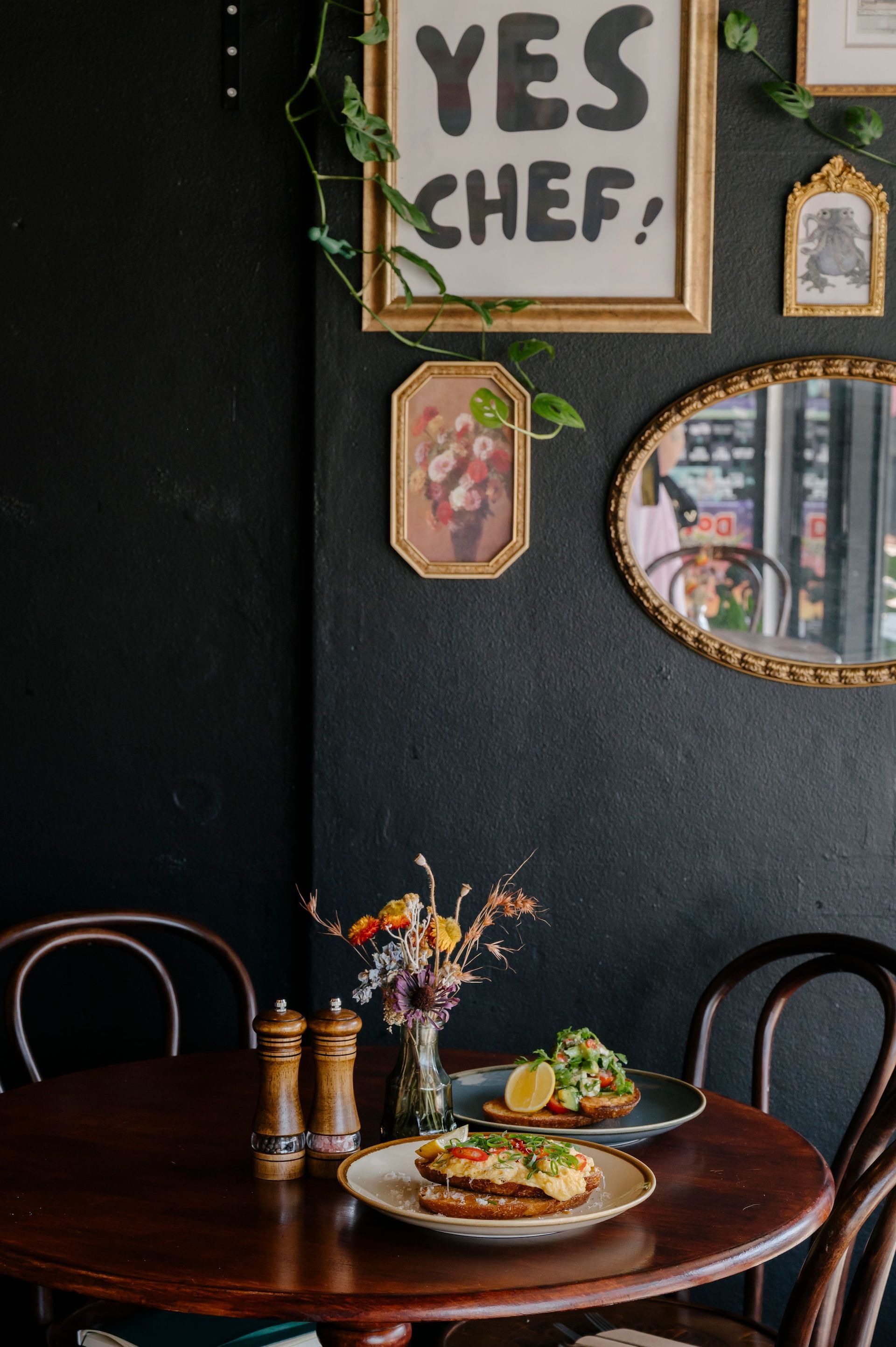 Dark dining room with round table, plates of food, and framed wall art — Drop In Espresso Bar in Wallsend, NSW