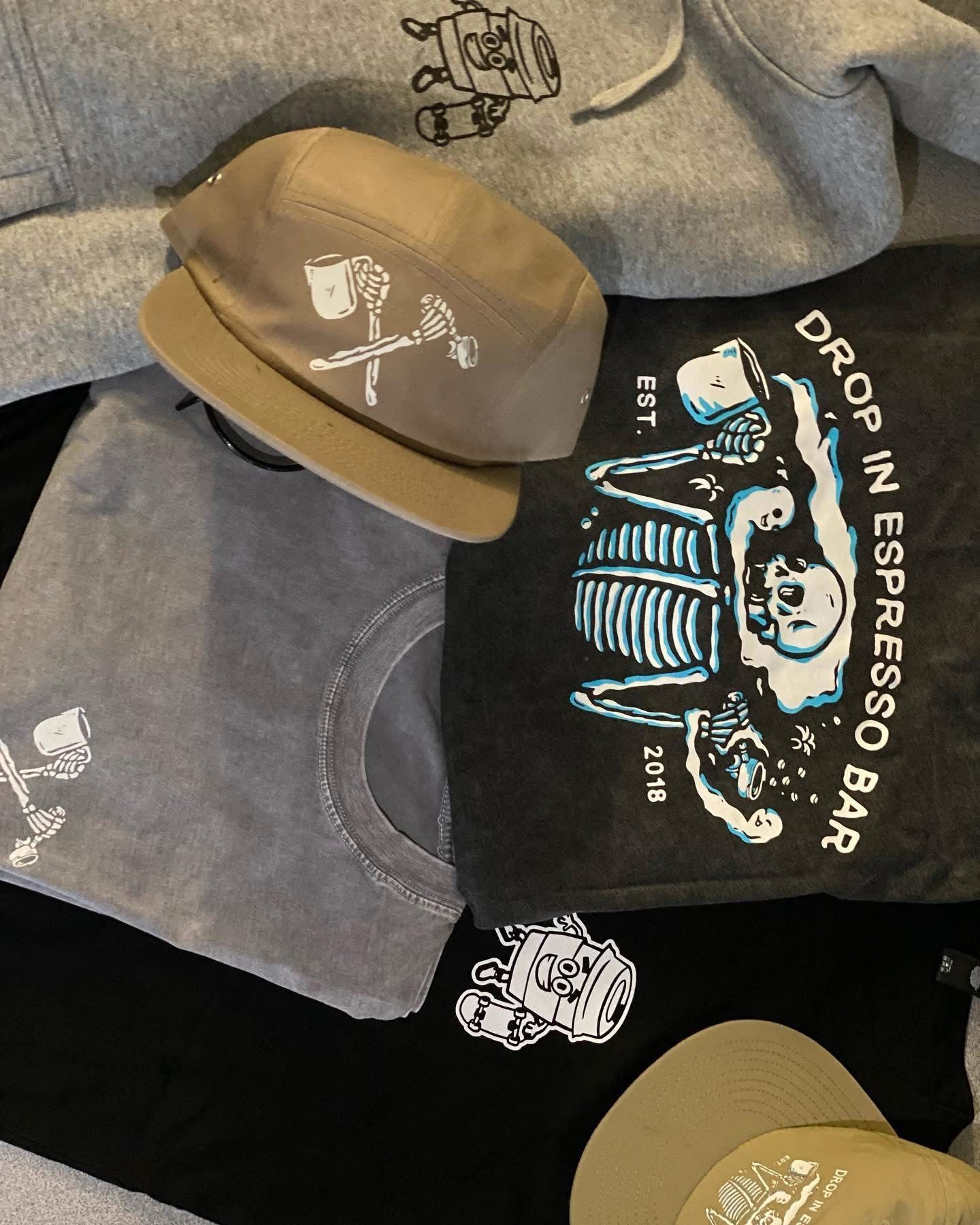 Apparel with coffee-themed skeleton logo. Gray hoodie, tees, and caps with graphic designs