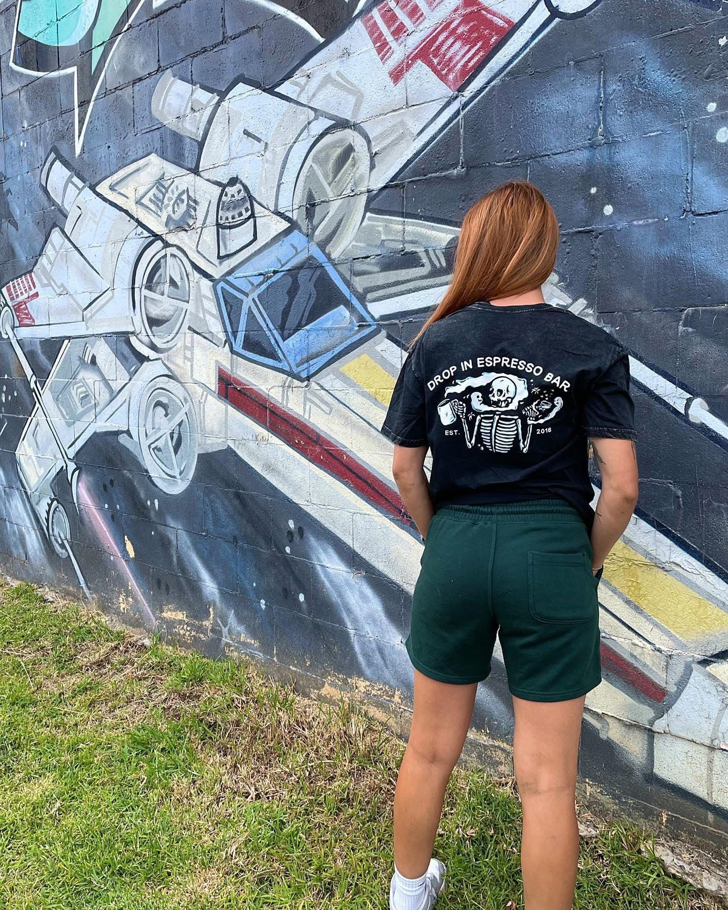 Woman in green shorts and black t-shirt with back to viewer poses in front of Star Wars graffiti — Drop In Espresso Bar in Wallsend, NSW