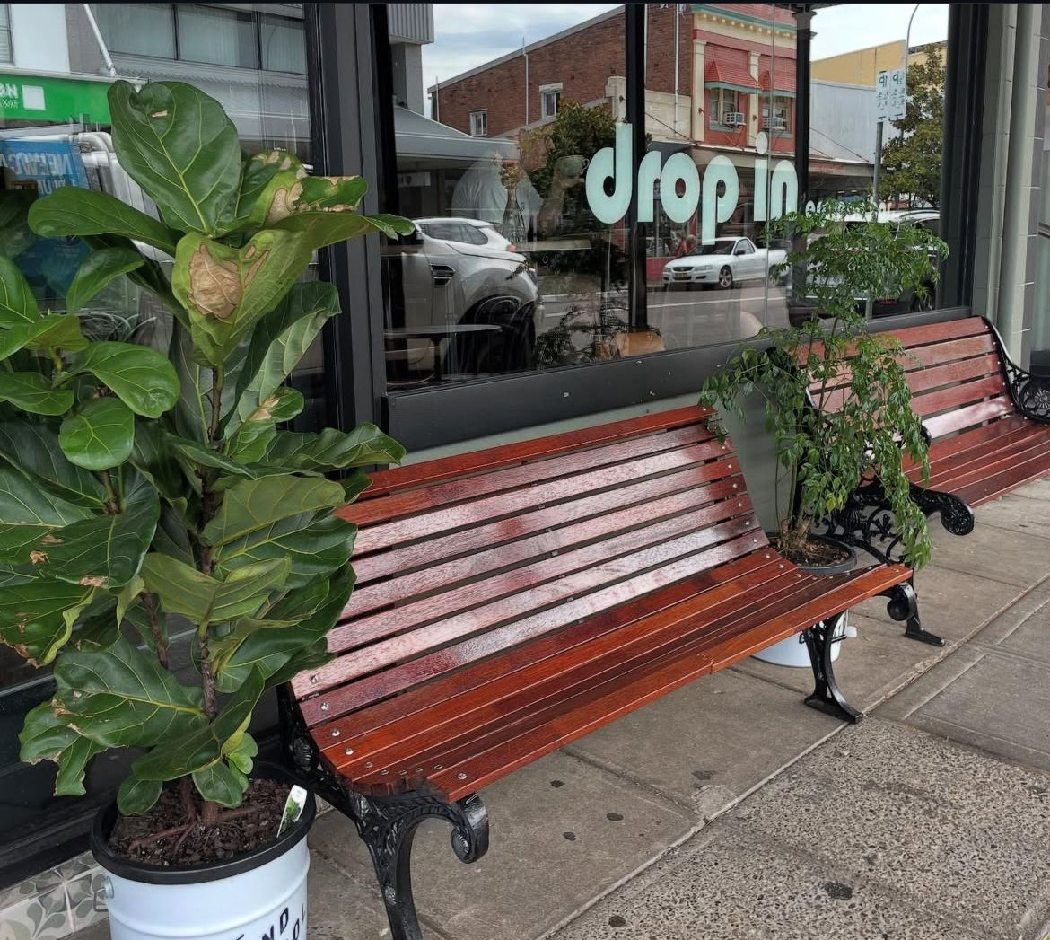 Sidewalk scene: two wooden benches, potted plants, storefront window with 