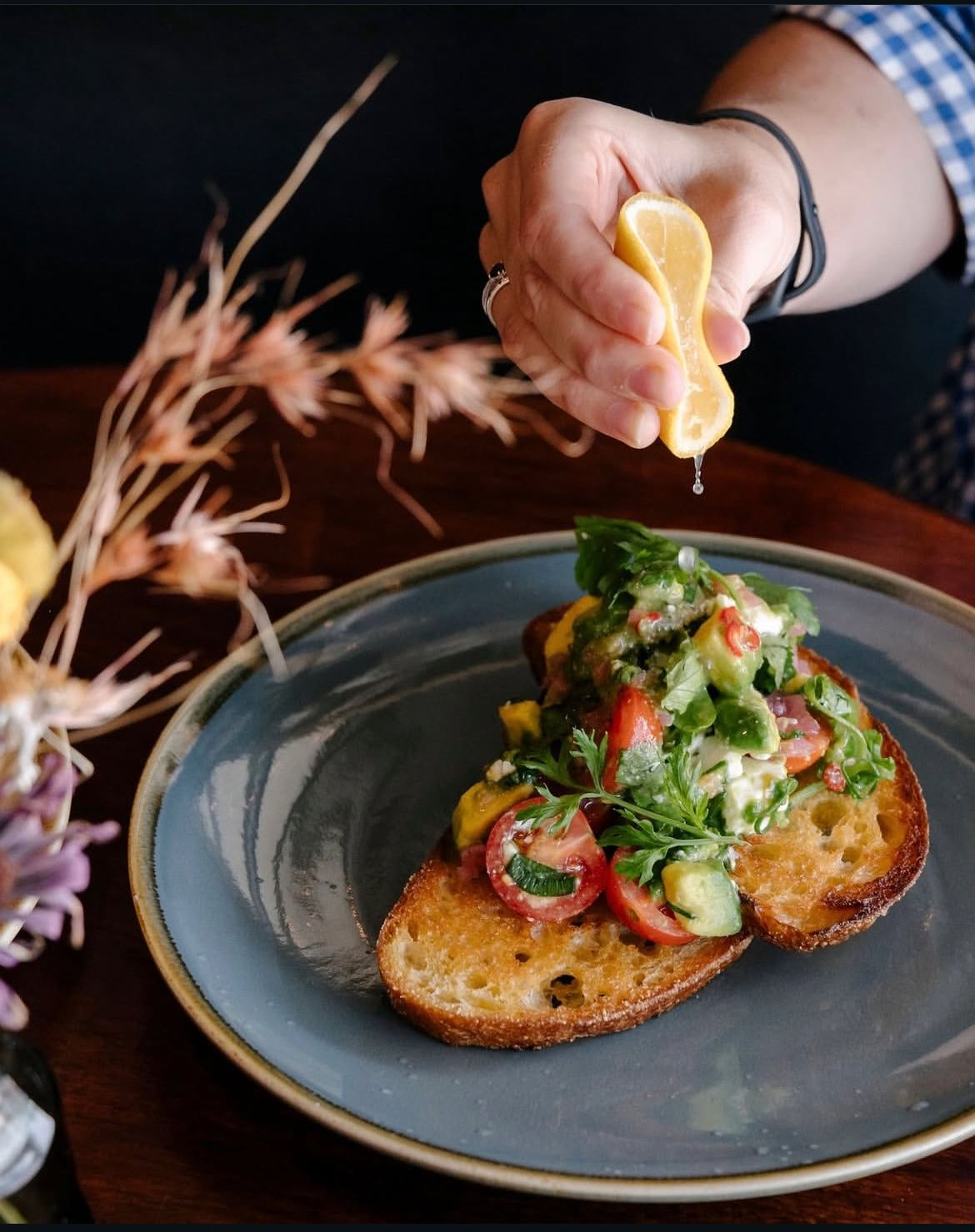 Person squeezing lemon over a tomato and cucumber bruschetta on a blue plate — Drop In Espresso Bar in Wallsend, NSW