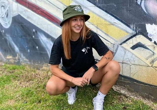 Woman in bucket hat and black shirt squats near graffiti wall — Drop In Espresso Bar in Wallsend, NSW