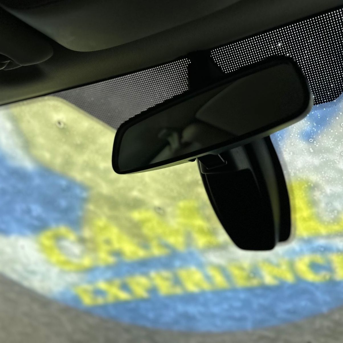 Interior car view with rearview mirror reflecting a colorful “Camel Experience” sign.