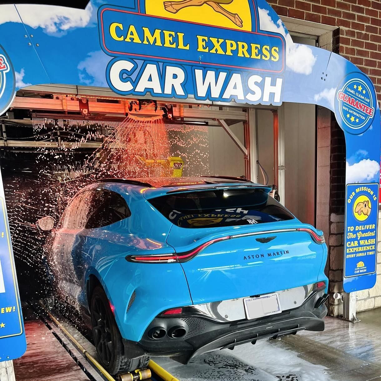 A light blue Aston Martin SUV is getting washed at a Camel Express Car Wash.