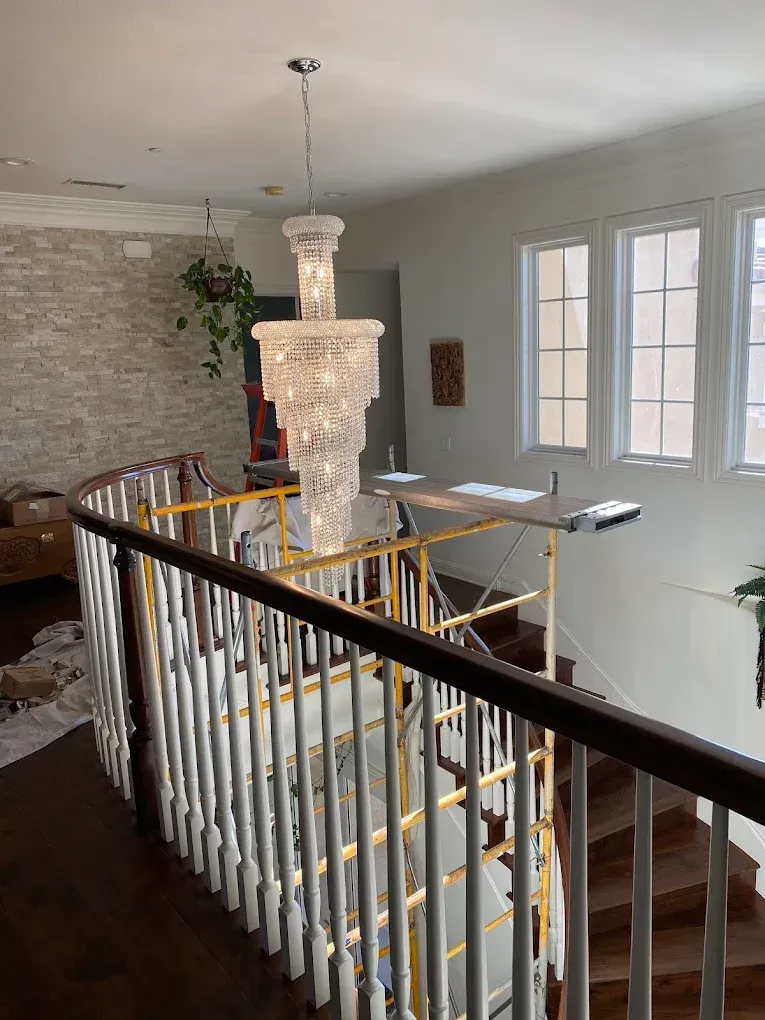 A staircase with white railings, wooden steps, and a large chandelier hangs from the ceiling.