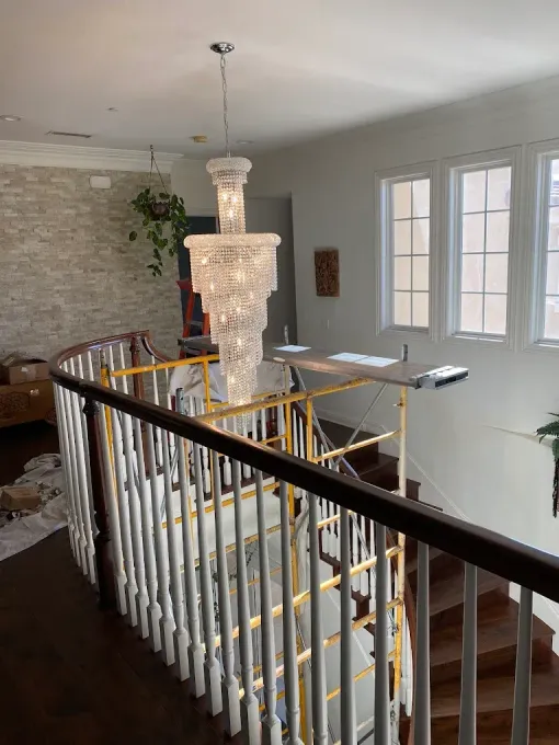 A staircase with white railings, wooden steps, and a large chandelier hangs from the ceiling.