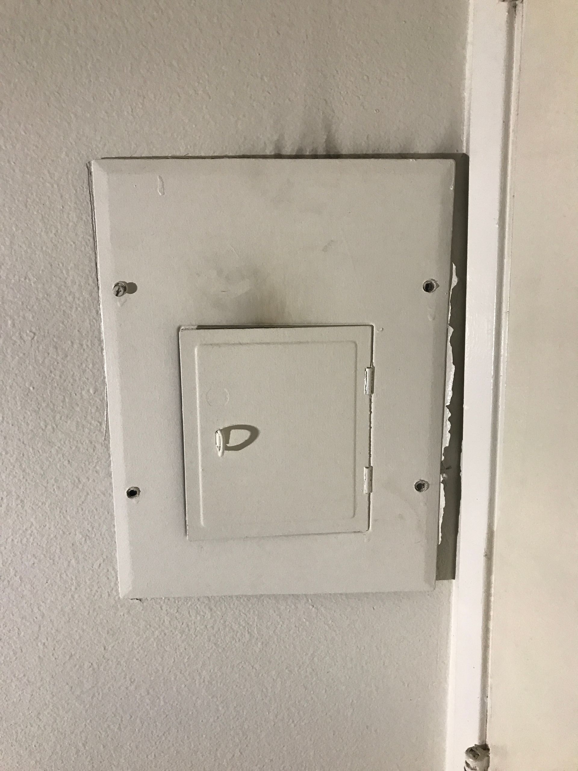 White electrical panel box with a smaller door on a light gray wall.