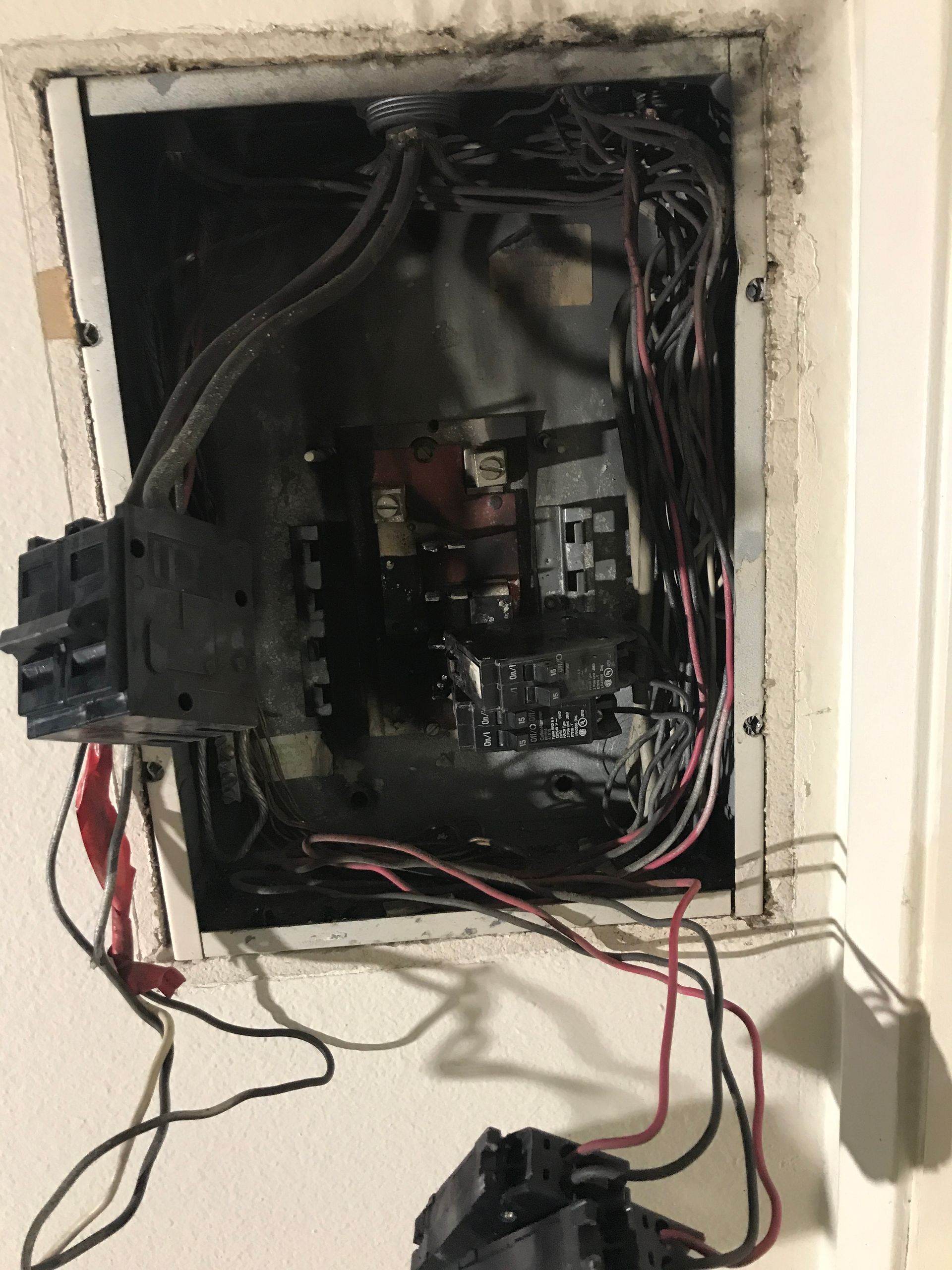 Burnt electrical panel in wall, wires exposed. Blackened interior, circuit breakers.