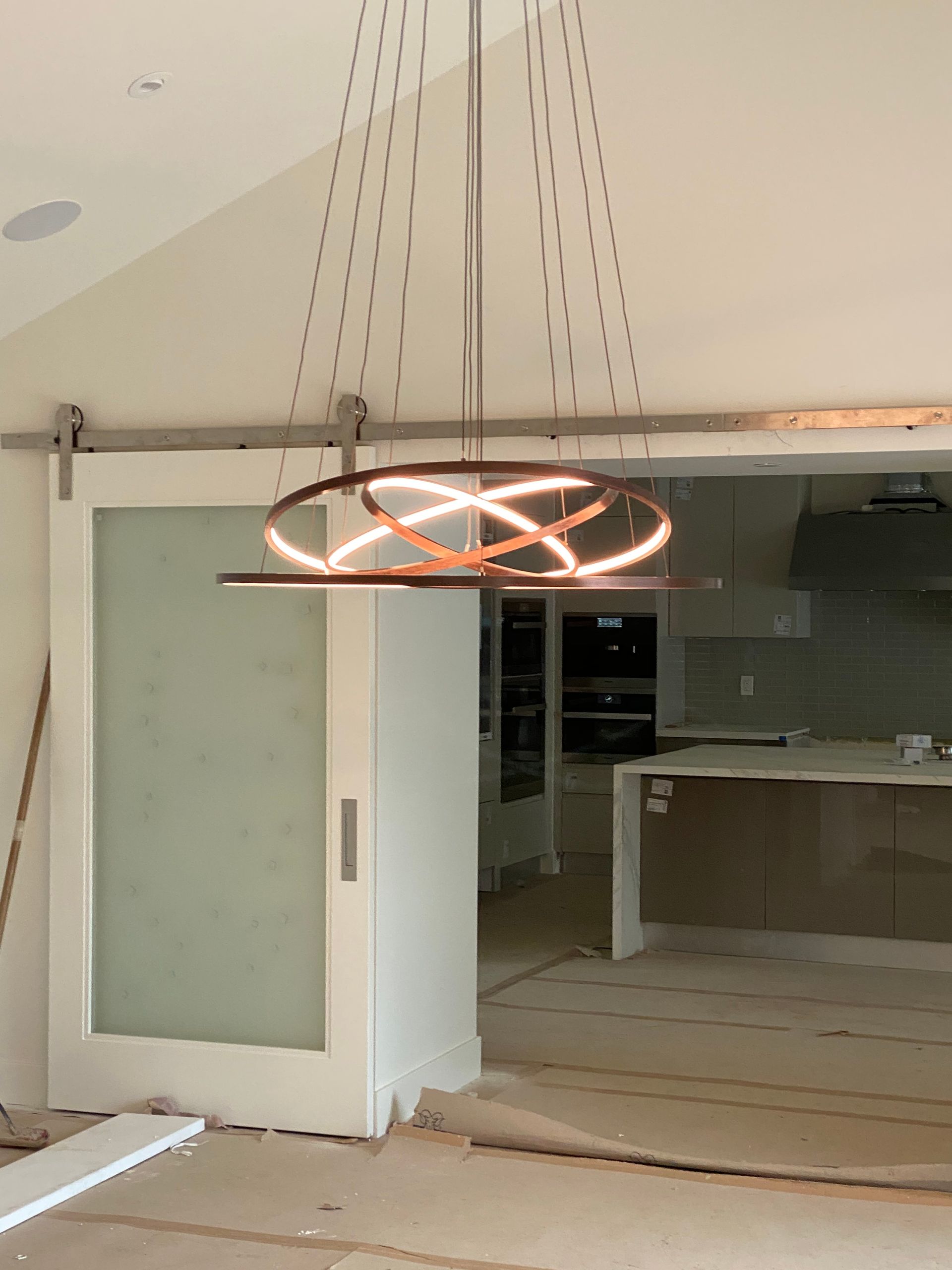 Modern copper-toned chandelier hanging above a frosted glass sliding door in a room under construction.