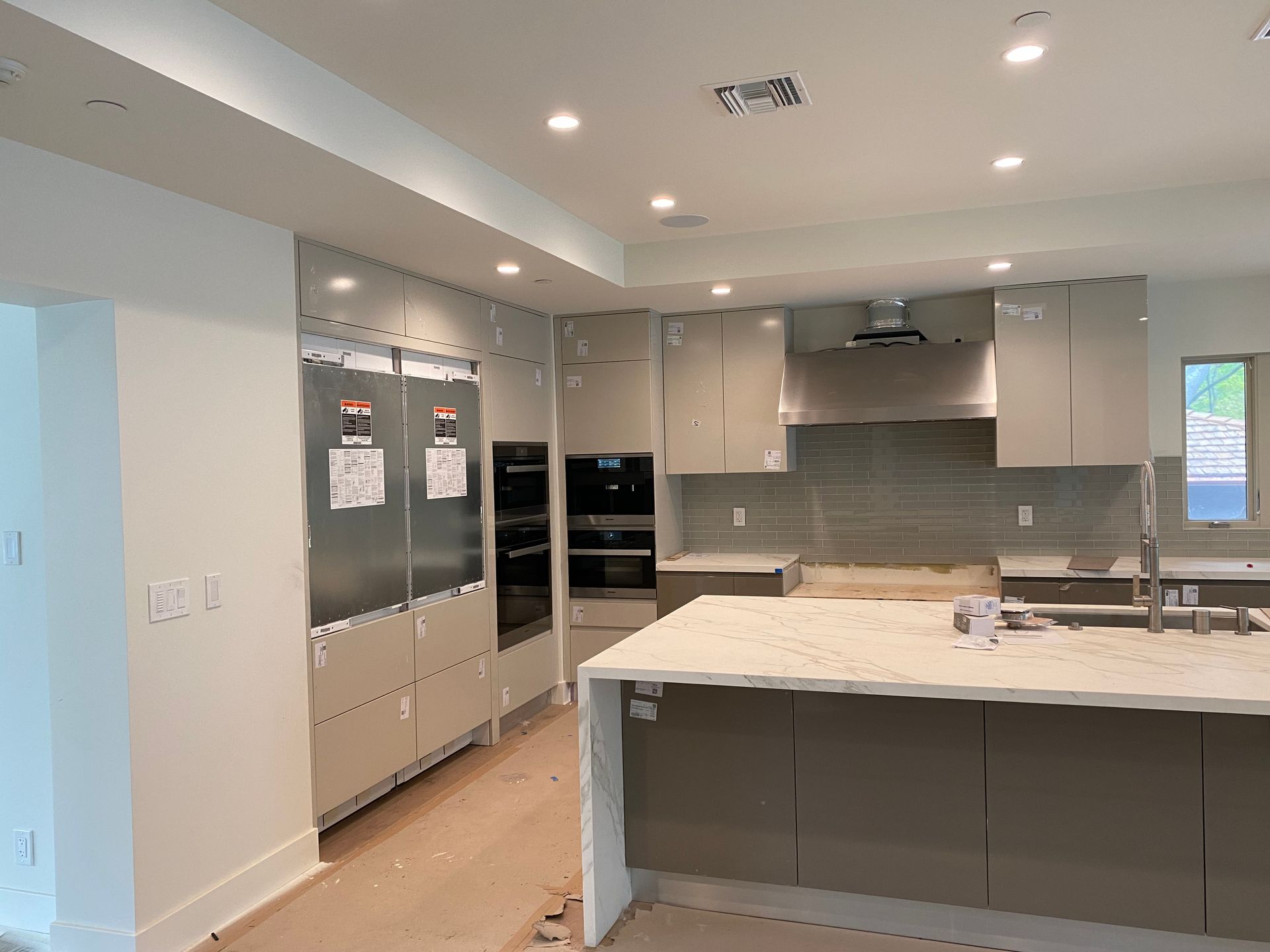 Modern kitchen with stainless steel appliances, light gray cabinets, and a white countertop island.