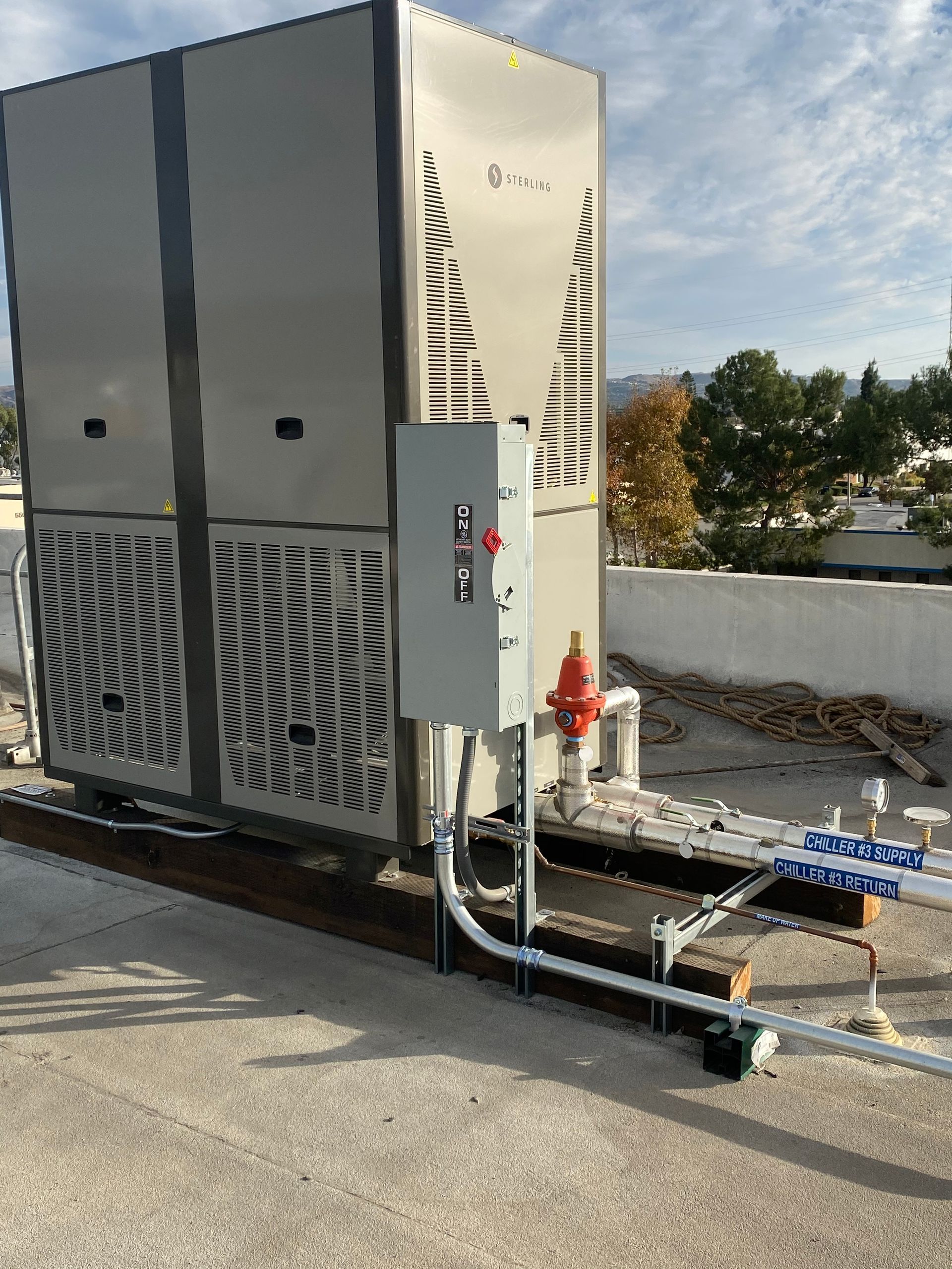 Large rooftop HVAC unit with electrical box and piping against a blue sky.