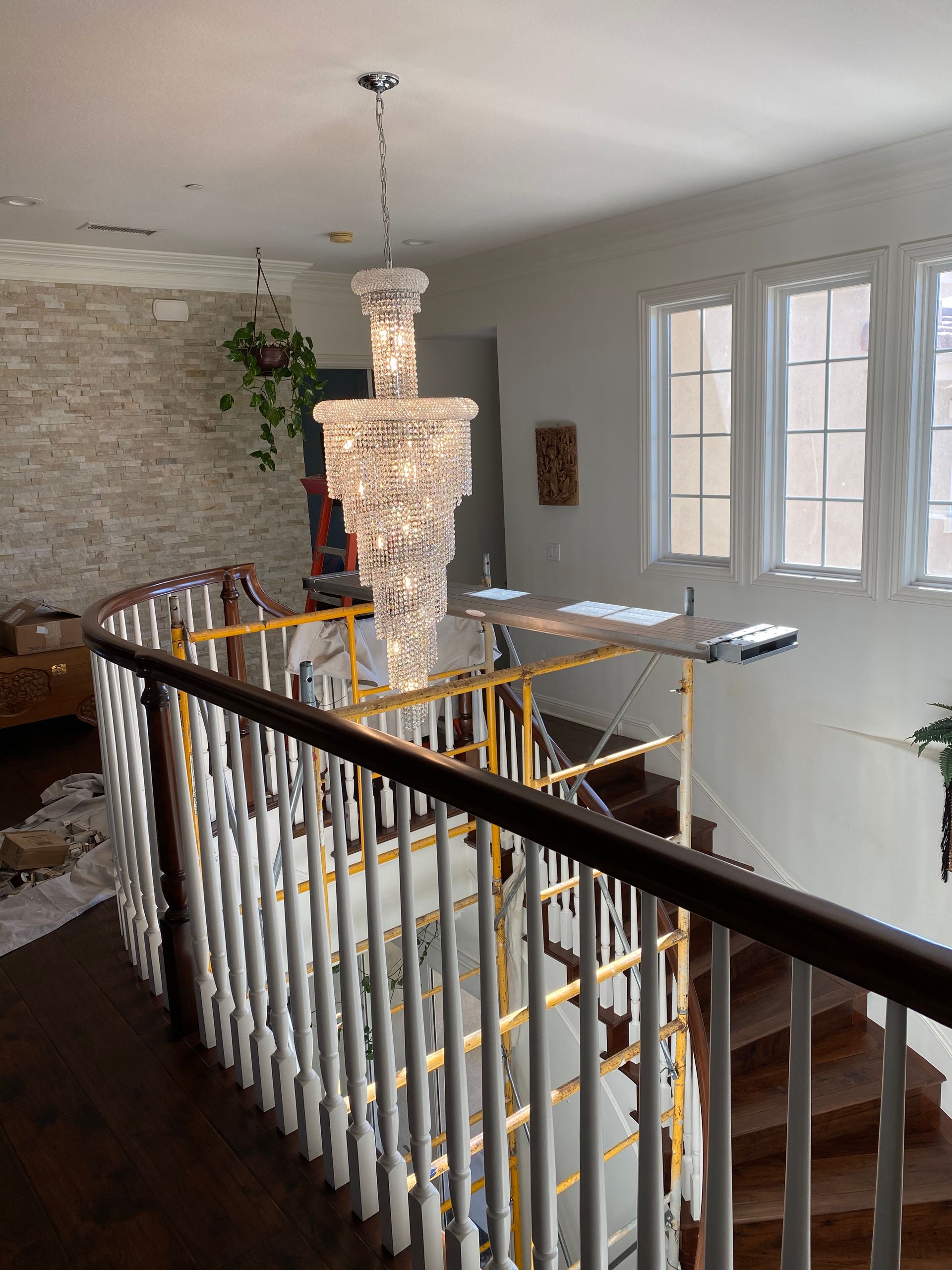 Chandelier hanging over a staircase. Yellow scaffolding, white walls, and brick accent wall.
