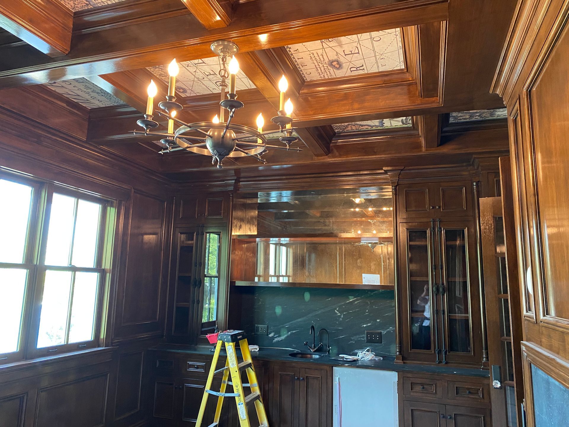 Dark wood-paneled room with a chandelier, bar area with a ladder and window.