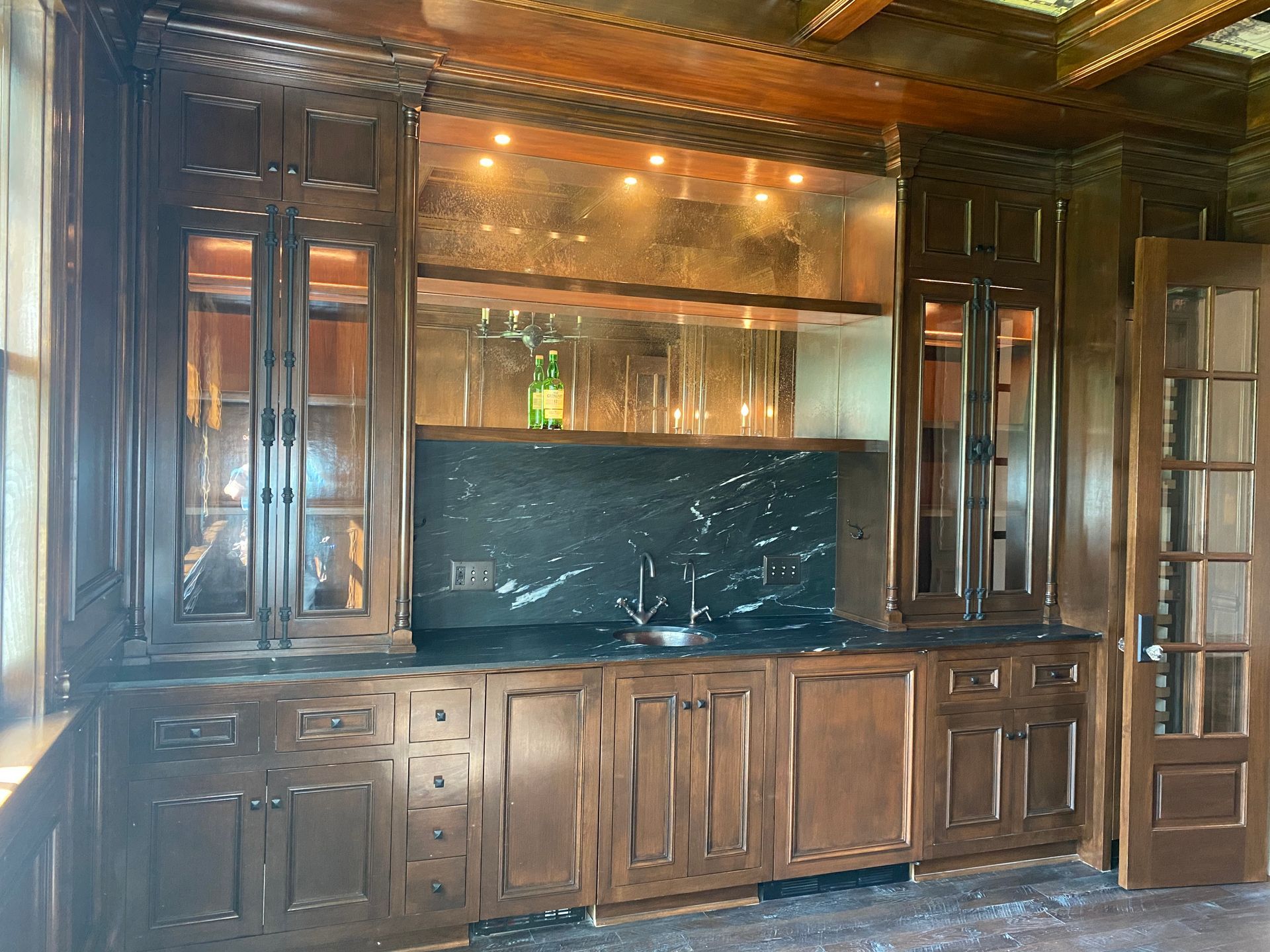 Dark wood wet bar with cabinets, a black marble backsplash, and a small sink.